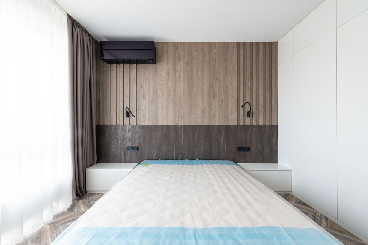 A photographed bedroom with a mattress and neutral furnishings